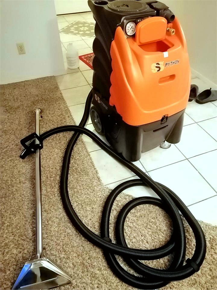 Orange SSS Python carpet extractor with its hose and stainless wand, set up at the edge of a carpeted room